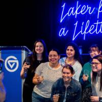 Group of grads smile with champagne in front of Laker for a Lifetime sign